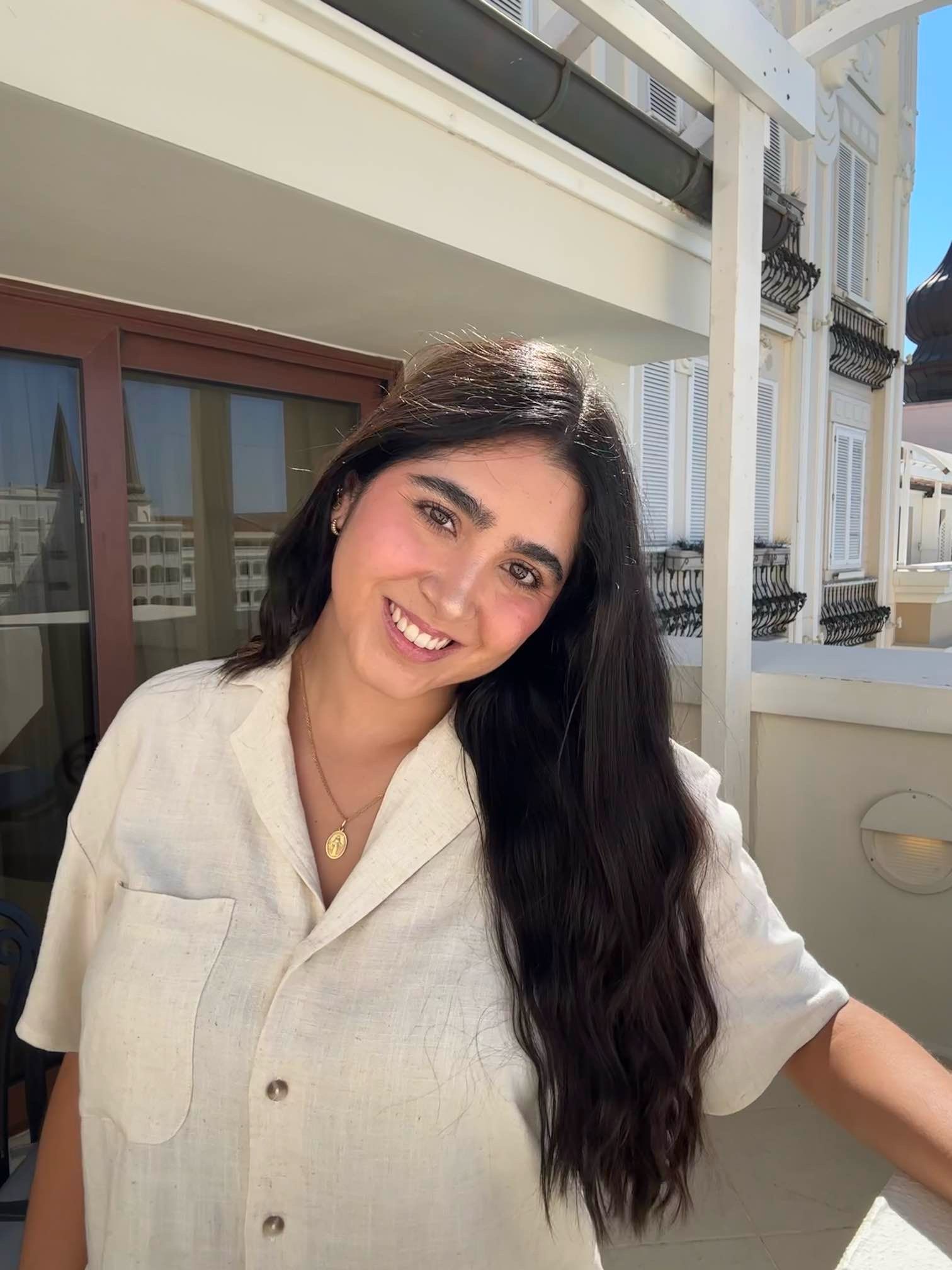 Photo of Sofia wearing a white t-shirt, smiling brightly in the sunshine on a balcony.